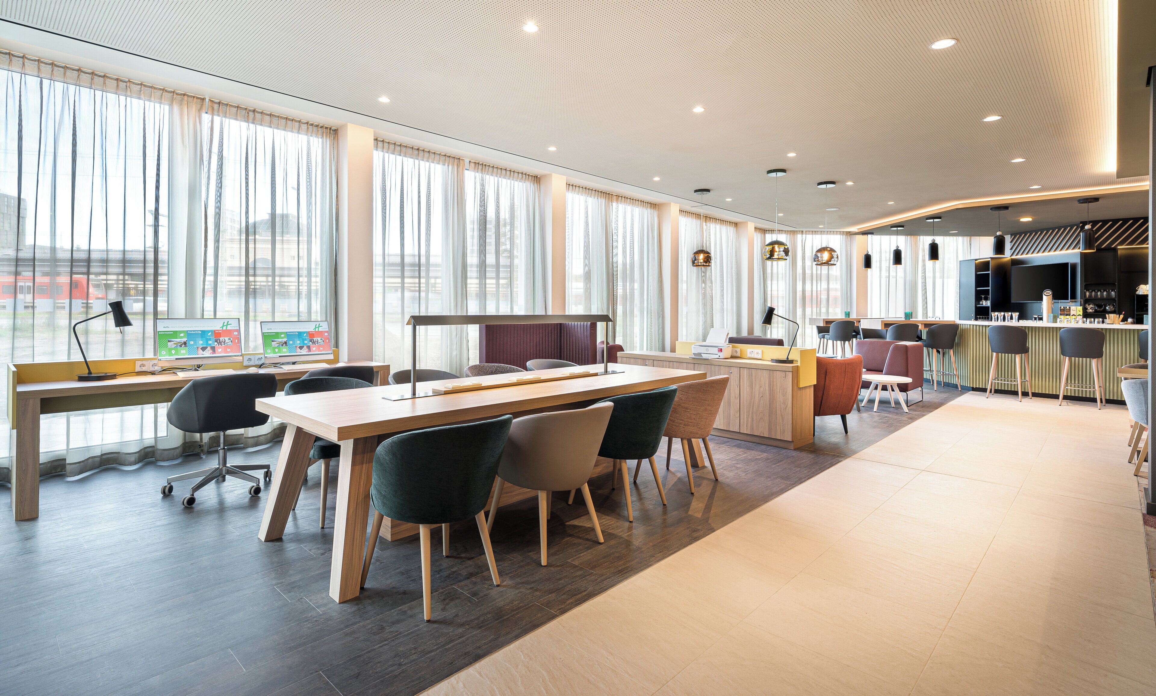 A modern office space with a long table, chairs, a desk with a computer, and a bar area with stools.