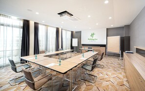 Un salón de conferencias con una mesa larga, sillas, una pizarra y una pantalla de proyector.