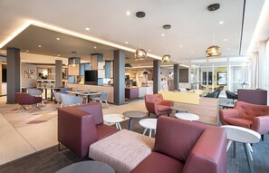 A modern hotel lobby with seating areas, a reception desk, and a dining space. - Holiday Inn Mannheim City - Hauptbahnhof by IHG (Mannheim)