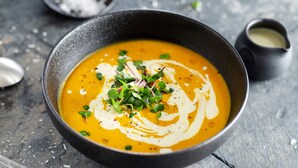 A bowl of soup with a creamy swirl on top, garnished with green herbs, on a rustic wooden table. - Holiday Inn Mannheim City - Hauptbahnhof by IHG (Mannheim)
