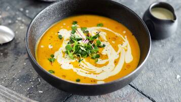 A bowl of soup with a creamy swirl on top, garnished with green herbs, on a rustic wooden table.