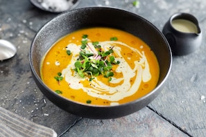 Un tazón de sopa con un remolino cremoso en la parte superior, adornado con hierbas verdes, sobre una mesa de madera rústica.