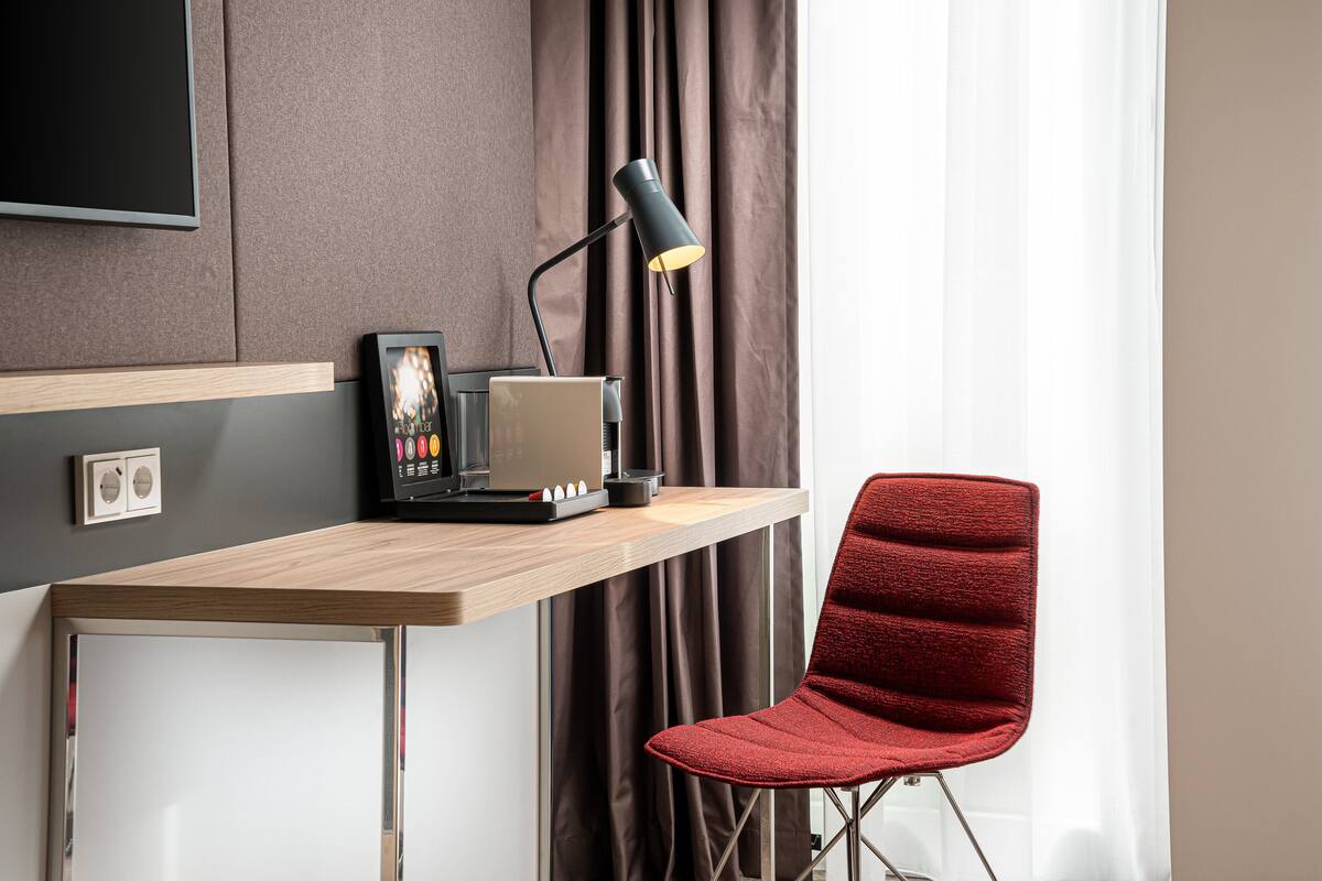 Ett modernt arbetsutrymme med ett skrivbord i trä, en röd stol, en svart lampa och en platt-TV som är monterad på väggen.