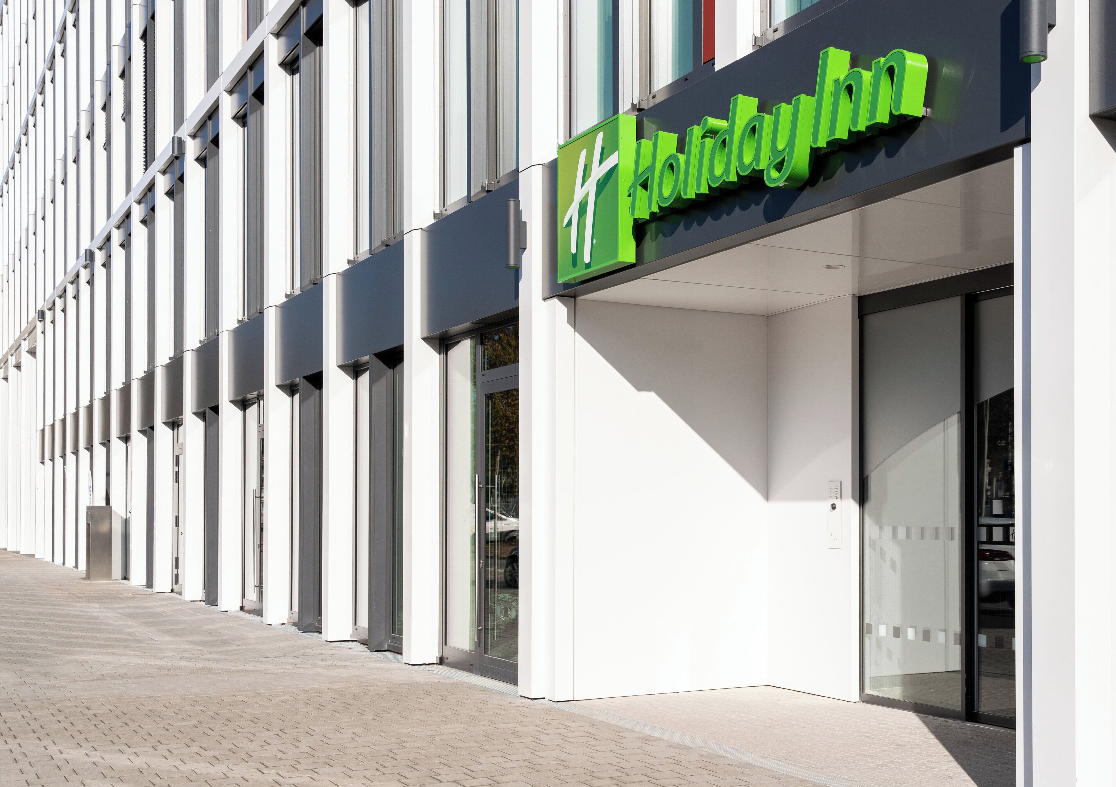 En modern byggnadsfasad med en tydlig grön skylt som visar att det är ett Holiday Inn-hotell.