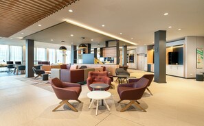 A spacious lobby with modern furniture, a bar area, and a kitchen visible in the background. - Holiday Inn Mannheim City - Hauptbahnhof by IHG (Mannheim)