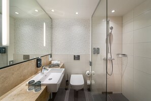 Un baño moderno con ducha de vidrio, lavamanos con espejo y retrete.