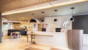 A modern hotel lobby with a reception desk, seating area, and a bar.