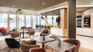 A modern cafe with tables and chairs, a bar area, and a refrigerator stocked with beverages.