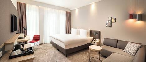 Una habitación de hotel moderna con cama, escritorio, silla, sofá y televisor.