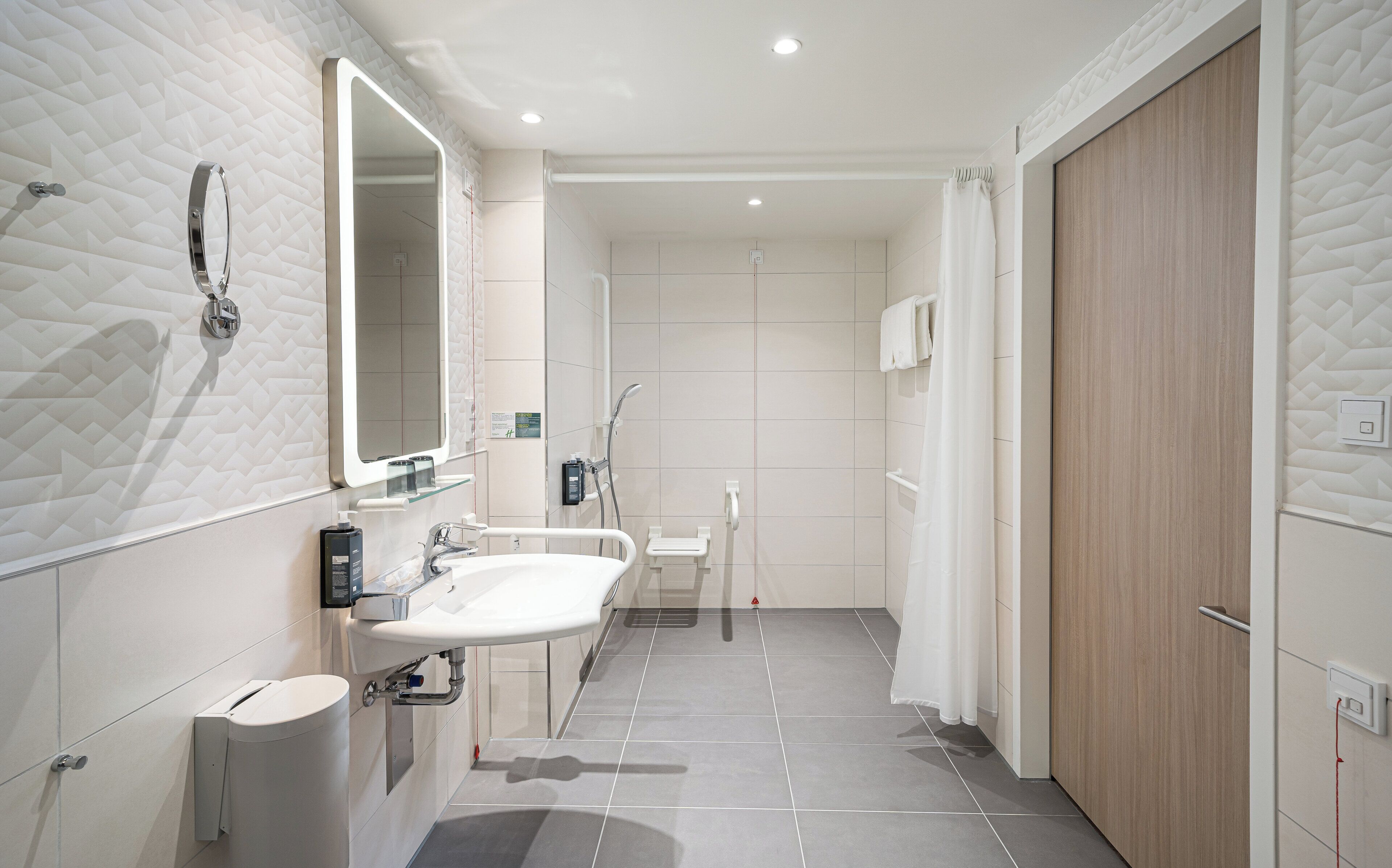 A modern bathroom with a large mirror, two sinks, a toilet, and a shower area.