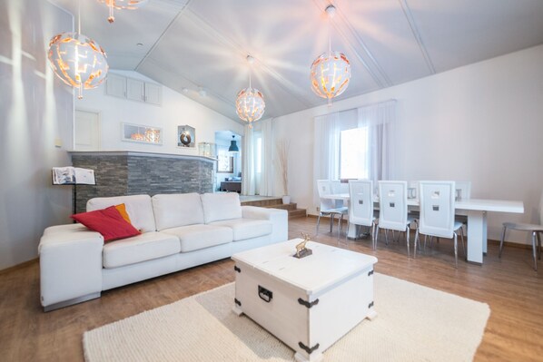 A modern living room with a white sofa, a white coffee table, and a dining area with white chairs and a table.