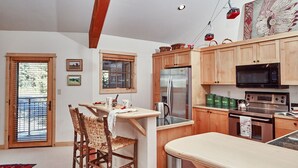 Une cuisine avec des meubles en bois, un réfrigérateur en acier inoxydable, un four à micro-ondes et une cuisinière. On y trouve une table à manger avec des chaises et une fenêtre avec des stores.