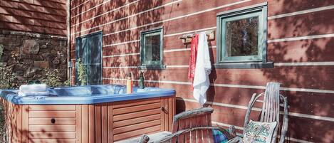 Un bain à remous en bois avec un couvercle bleu, une chaise en bois rustique et un mur de pierres en arrière-plan.