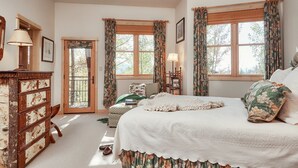 Une chambre avec un grand lit, une commode, une chaise et deux fenêtres avec des rideaux.