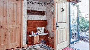 Une pièce chaleureuse avec un banc en bois, une petite table sur laquelle sont posés quelques objets, un panier et une porte donnant sur l’extérieur.