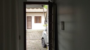 A room with a tiled floor, a white door leading outside, and a white chair in the foreground. - Studio apartment in a condominium with air conditioning. (Curitiba)