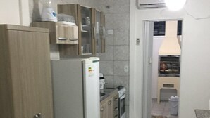A compact kitchen with a refrigerator, stove, and cabinets. - Studio apartment in a condominium with air conditioning. (Curitiba)