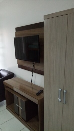A room with a wooden TV stand, a mounted flat-screen TV, a remote control, and a closed wardrobe.
