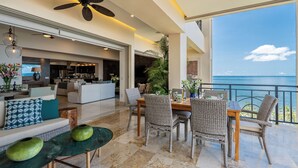 Un vaste espace de vie comprenant une table à manger, des chaises en osier et une vue sur l’océan.