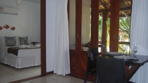 A room with a bed, a dining table with chairs, and a view of the outdoors. - Bahia Bonita Flat (Itacaré)