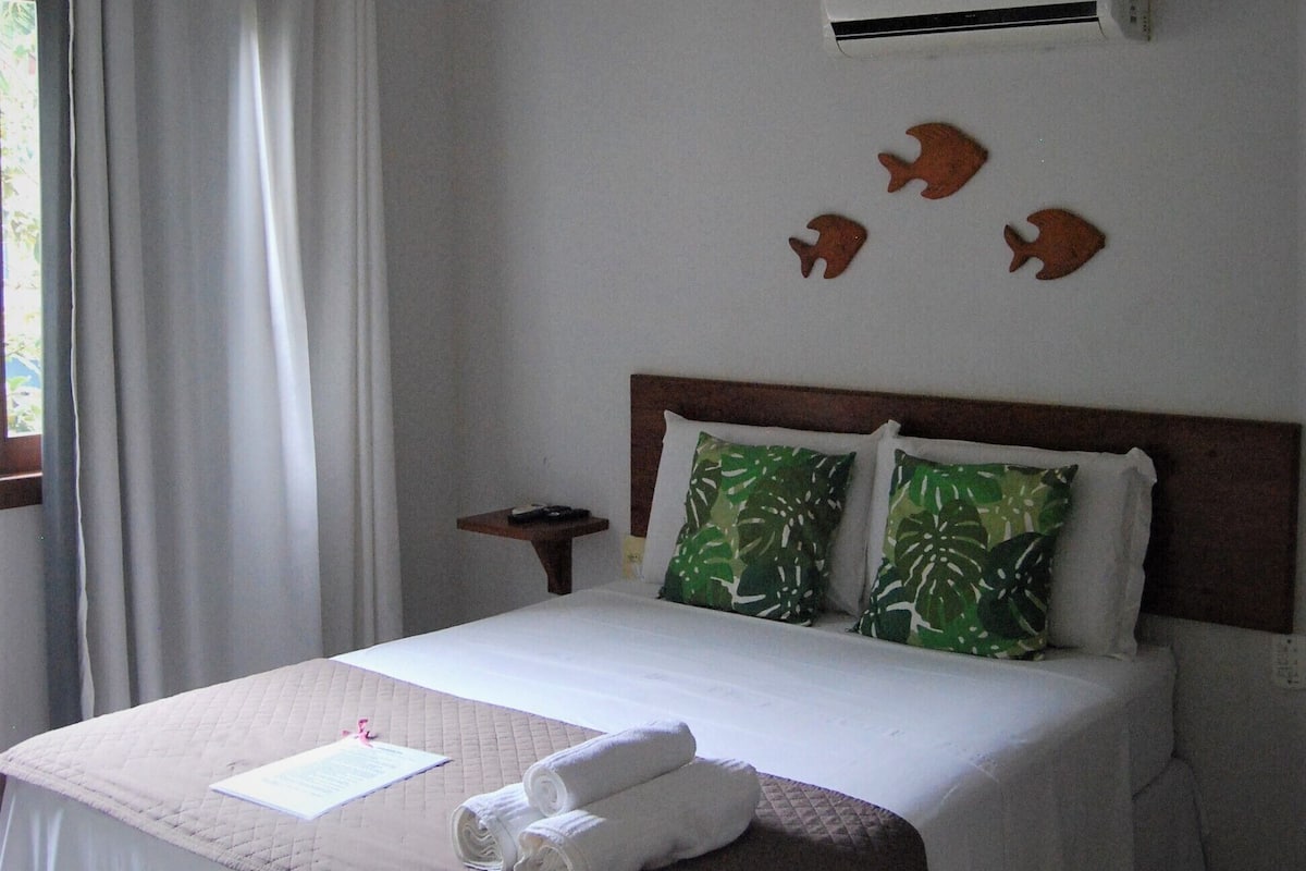 Une chambre d’hôtel avec un lit, un ventilateur de plafond, un climatiseur et une fenêtre avec des rideaux.