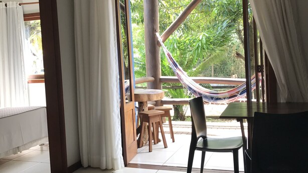 A room with a view of greenery, a hammock, and a dining area with chairs and a table. - Bahia Bonita Flat (Itacaré)