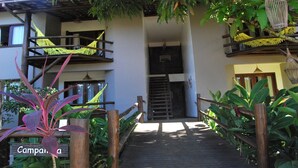 A wooden pathway leading to a building with balconies and hammocks. - Bahia Bonita Flat (Itacaré)