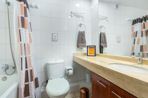 A modern bathroom with a white tiled wall, a beige countertop, a white toilet, and a shower curtain with a geometric pattern. - Perfect Apartmen For Lover Of Travels. Best Located, Full Equiped, Include A/C! (Santiago)