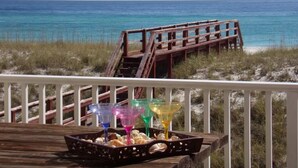 A wooden deck with a railing, a beach view, and colorful cocktail glasses on a tray. - Bright Sands-Gulf Front Home with Private Crossover (Navarre)