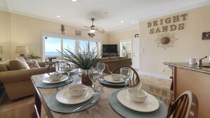 A dining area with a table set for four, a ceiling fan, and a view of the ocean through a large window. - Bright Sands-Gulf Front Home with Private Crossover (Navarre)