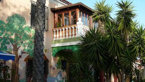 Ein Gebäude mit Balkon, Palmen und einem Wandbild von Baum und Vogel.