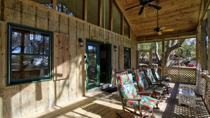 A covered porch with wooden walls and a ceiling fan, featuring rocking chairs and a lattice railing. - Sound View, Pet Friendly Home in Harkers Island, NC (Core Sound Lodge) (Harkers Island)