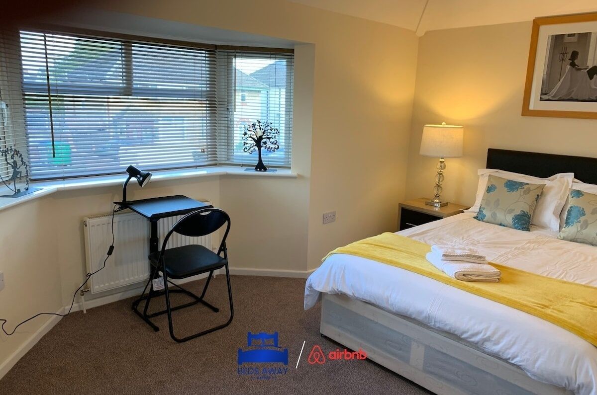 Un dormitorio con cama, escritorio, silla, ventana con persianas, radiador y lámpara.