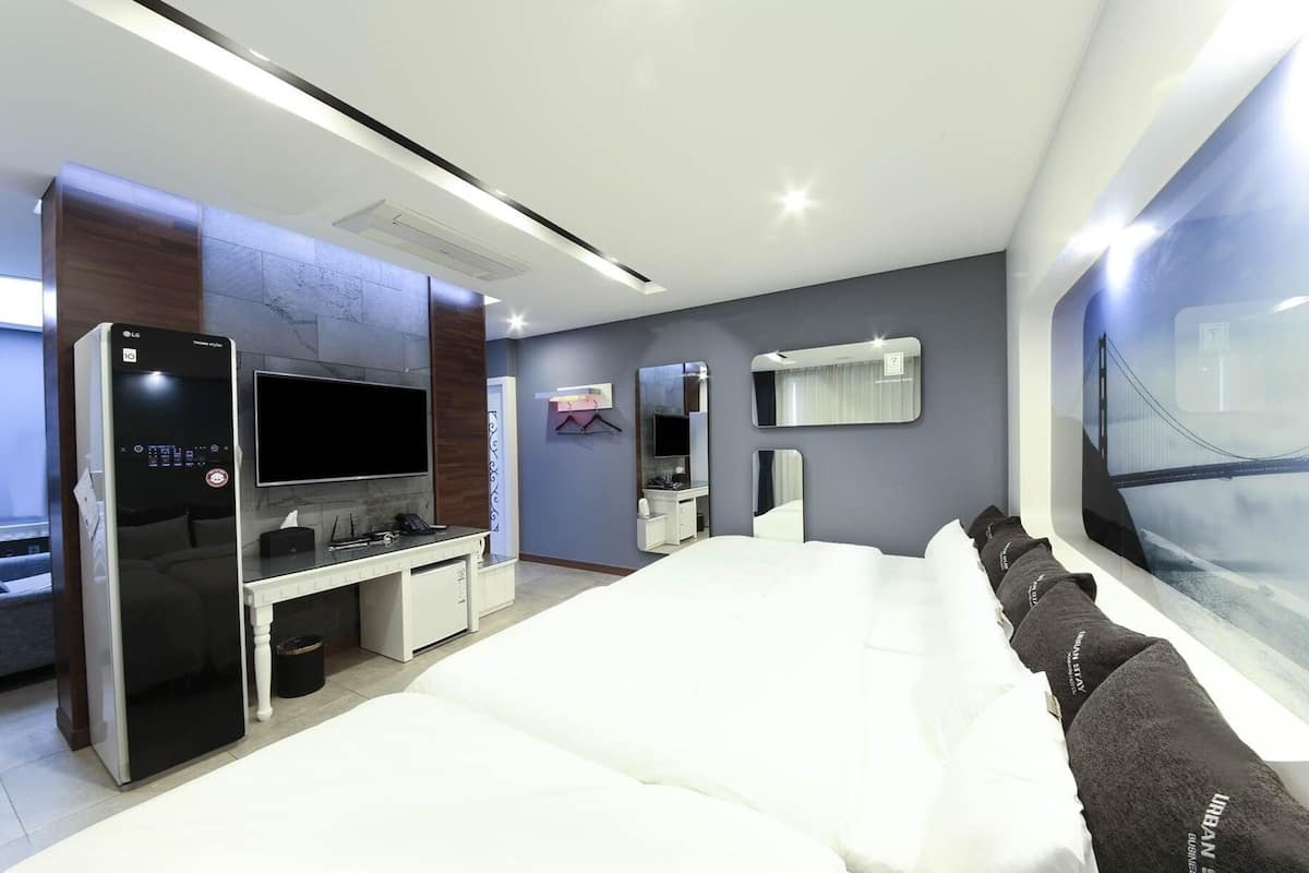 Una habitación de hotel moderna con una cama grande, un televisor de pantalla plana, un escritorio con una computadora, un espejo y una ventana con vista a la ciudad.