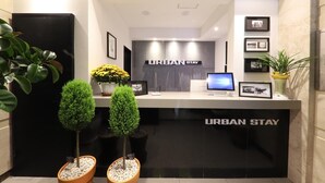 A reception desk with "URBAN STAY" signage, framed pictures on the wall, and two potted plants. - Urban Stay (Gwangju)