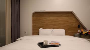 Ein Hotelzimmer mit Holz-Kopfteil, weißer Bettwäsche, einem Tablett mit Tasse und Zeitschrift sowie einem Blumenkorb.