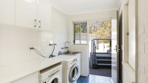 A compact laundry room with a washing machine, a sink, and a window providing a view of the outside. - Bayview Ringlands - Enjoy this relaxing escape (Narooma)