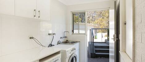 A compact laundry room with a washing machine, a sink, and a window providing a view of the outside.