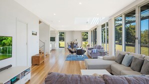 A spacious living room with a large TV, a sofa, and a dining area with a table and chairs. - Bayview Ringlands - Enjoy this relaxing escape (Narooma)