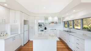 A modern kitchen with white cabinetry, stainless steel appliances, and a large window providing a view of the outdoors. - Bayview Ringlands - Enjoy this relaxing escape (Narooma)