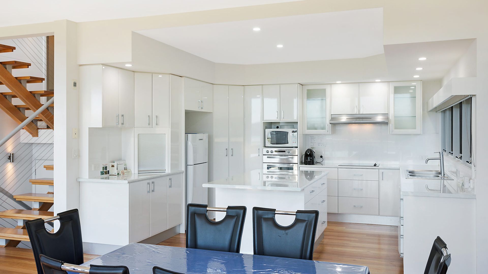 Una cocina moderna con armarios blancos, una isla central y una zona de comedor con mesa y sillas.