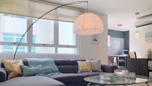 Ein modernes Wohnzimmer mit einer Eckcouch, einem Glastisch und einem großen Fenster, das für natürliches Licht sorgt.