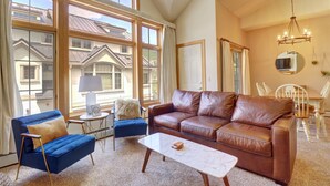 A spacious living room with a brown leather sofa, a blue armchair, and a white coffee table. Large windows offer a view of neighboring houses. - Pet Friendly, Slope-side, Spacious Town Home  ER21 (Copper Mountain)