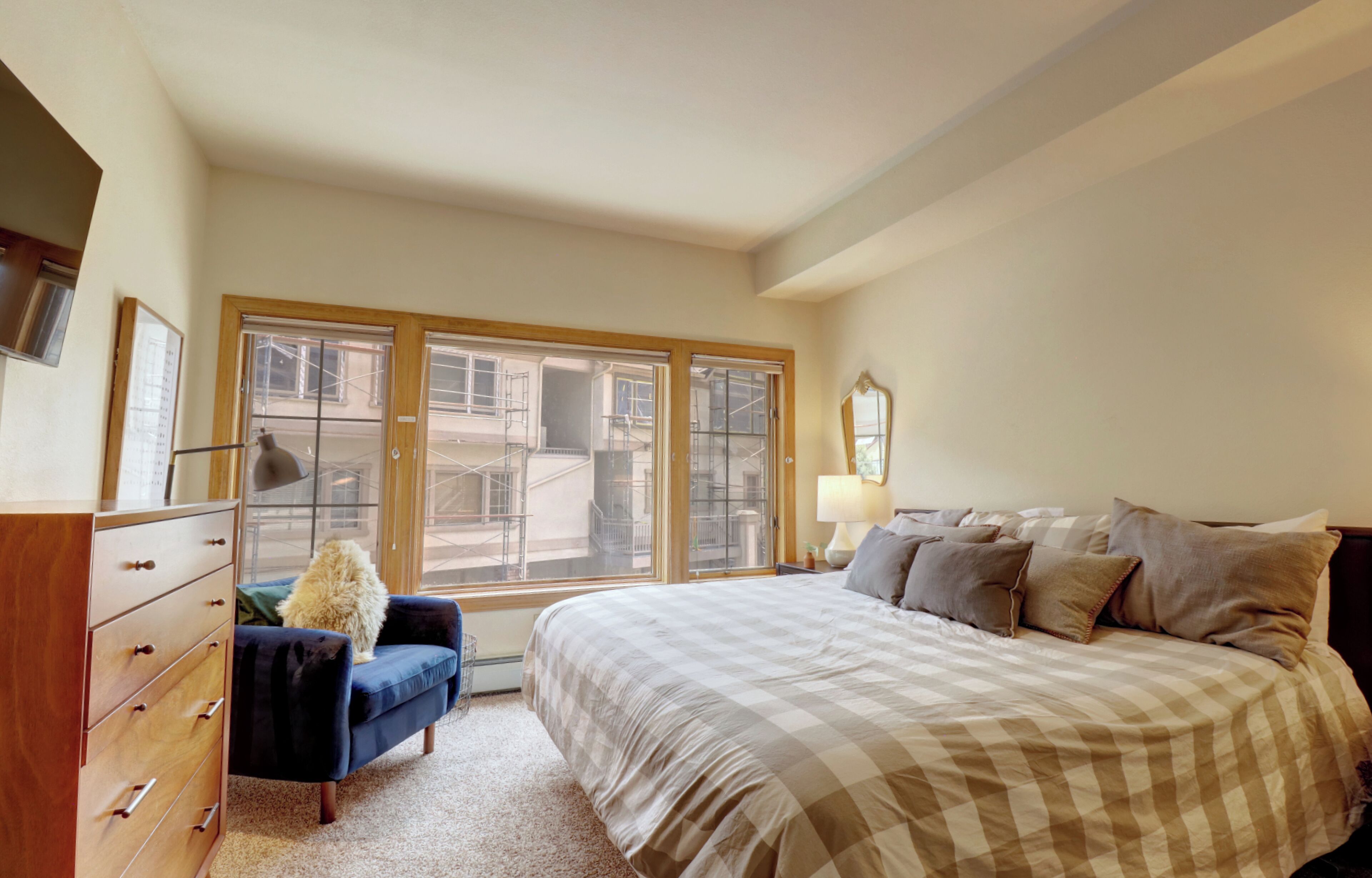 Ein Schlafzimmer mit einem großen Bett, einem Schminktisch, einem Sessel und einem Fenster mit Blick auf Gebäude.