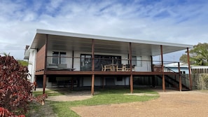 A modern two-story house with a covered balcony and a visible staircase. - JJ s Holiday House - River views and ocean breezes await (WOOLI)
