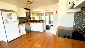 A modern kitchen with white cabinetry, a built-in dishwasher, and a black backsplash. - JJ s Holiday House - River views and ocean breezes await (WOOLI)