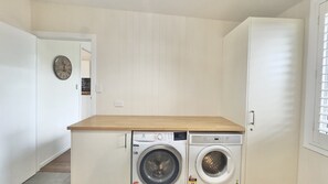Una piccola zona lavanderia con lavatrice e asciugatrice, un piano di lavoro in legno e una sveglia appesa al muro.
