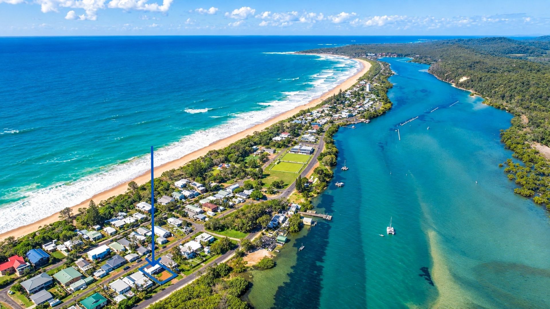 An aerial view of a coastal area with a beach, residential buildings, and a clear blue sea.