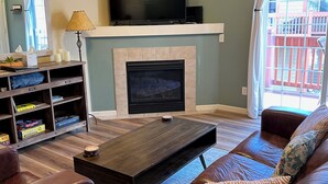 Una sala de estar con chimenea, un televisor sobre un mueble bajo, un sofá y una mesa de centro.