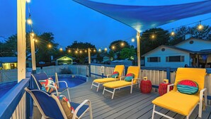 En terrasse med liggestole og swimmingpool, omgivet af et træhegn og lyskæder.